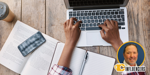 Image of a workspace with an open book, phone and person typing on a computer Image of a workspace with an open book, phone and person typing on a computer